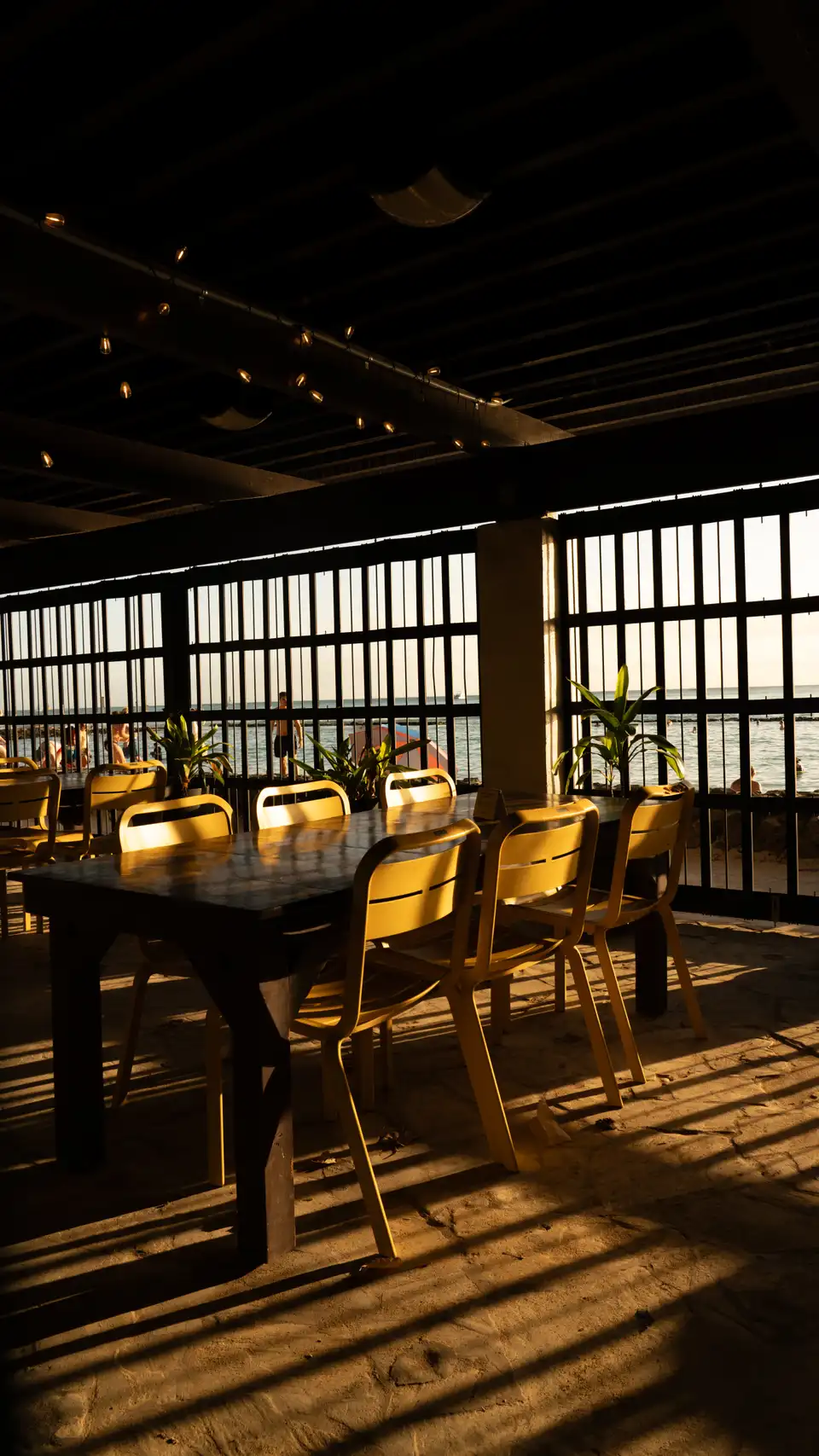 Indoor window view in Waikiki, Hawaii, with dining tables, slats, and beachgoers outside.