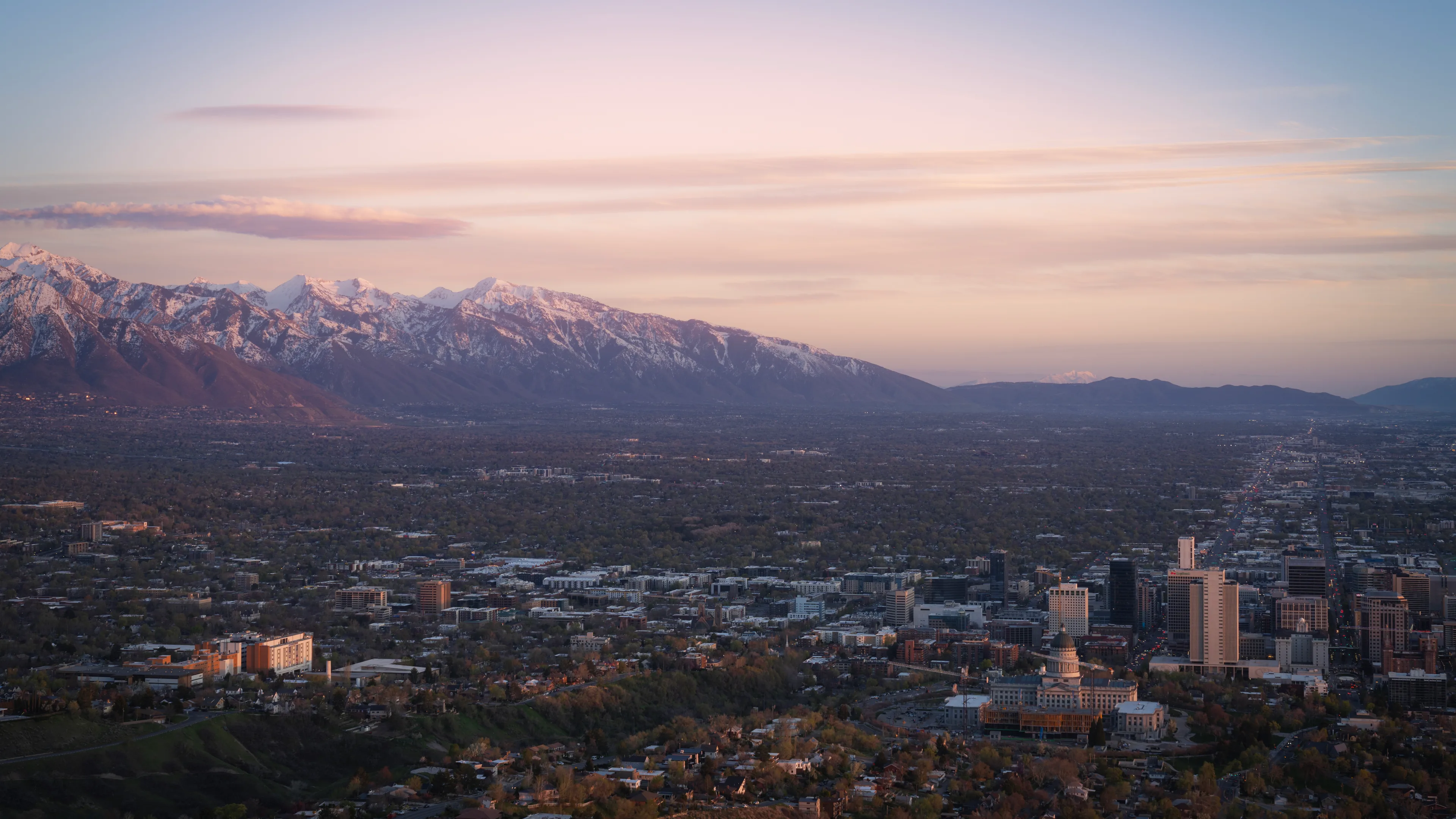 Salt Lake City skyline at dusk from Ensign Peak, with valley lights and distant mountains.