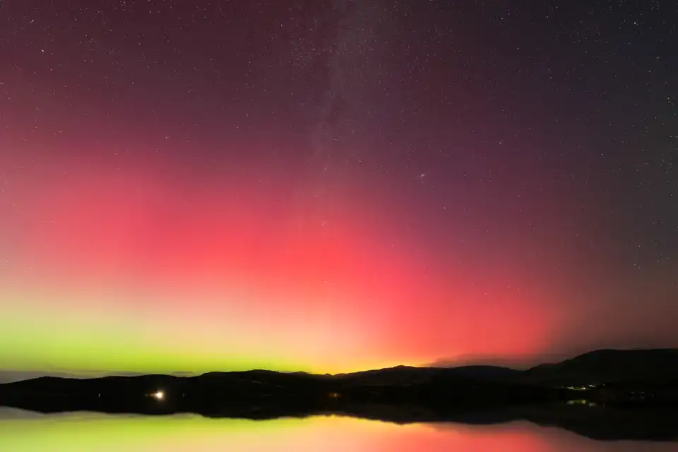 Red and green aurora above Rockport Reservoir, with shoreline and hills below.