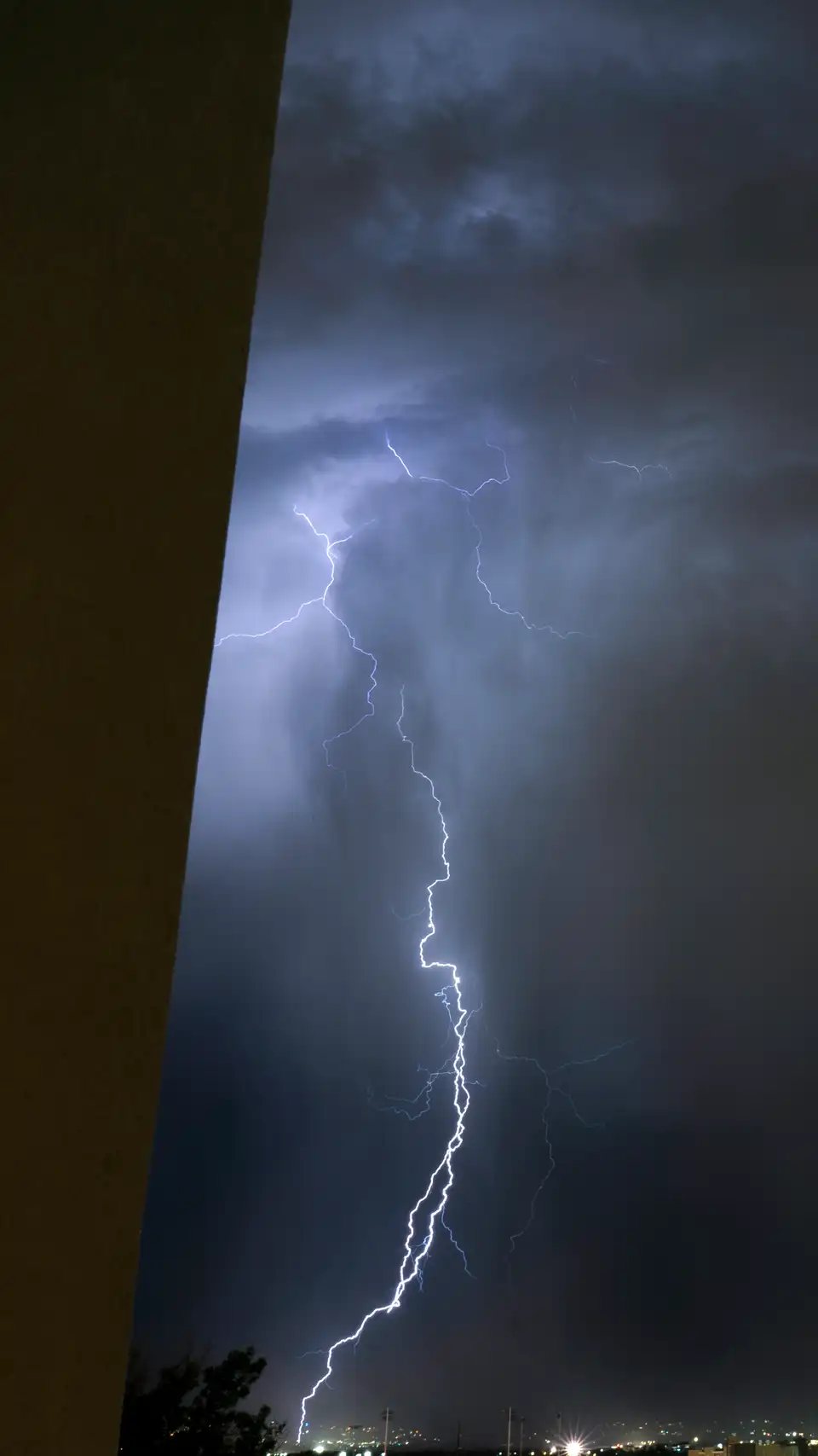 Lightning in the night sky over Salt Lake City, with city lights and mountain outlines below.