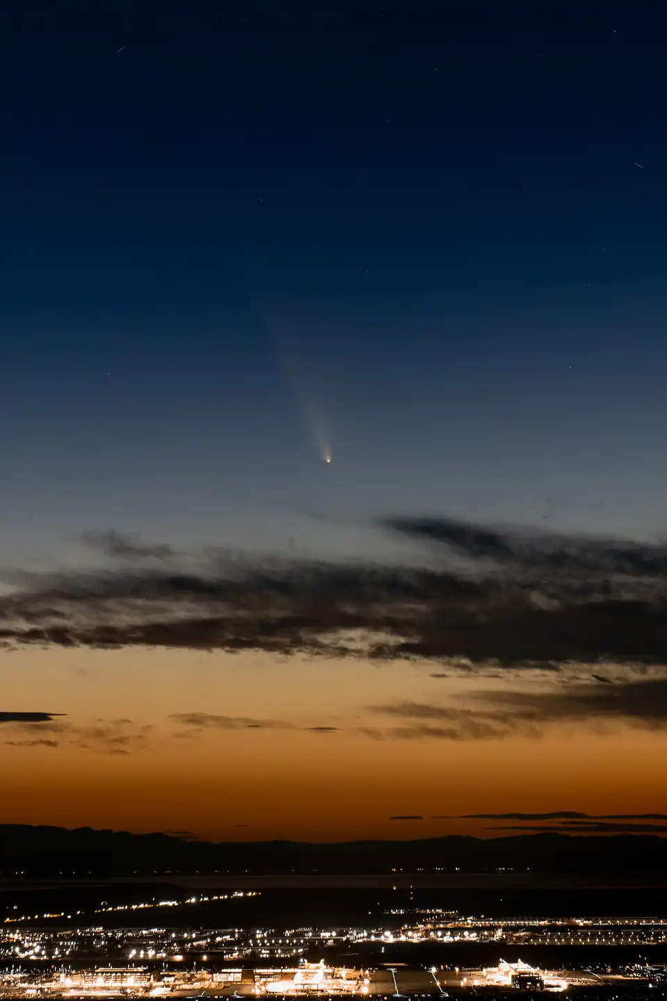 Comet above the Salt Lake City skyline at night, with city lights below.